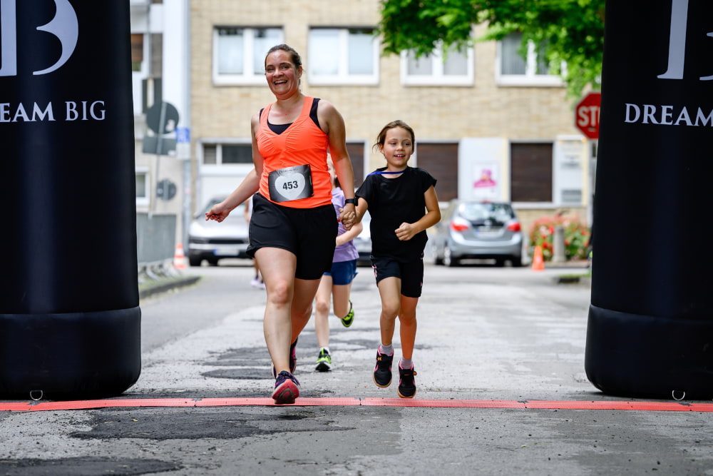 Eine Erwachsene und ein Kind überqueren gemeinsam die Ziellinie beim Sportfest Move & Groove.