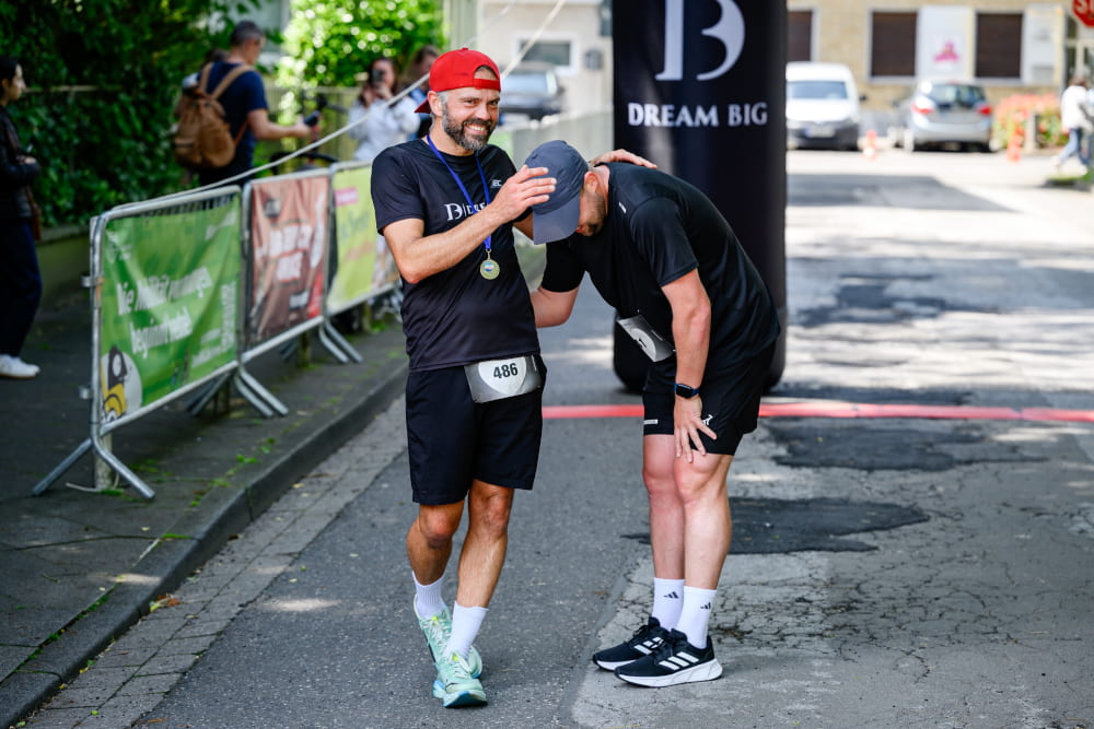 Ein Teilnehmer unterstützt einen erschöpften Läufer nach dem Zieleinlauf beim Sportfest Move & Groove.
