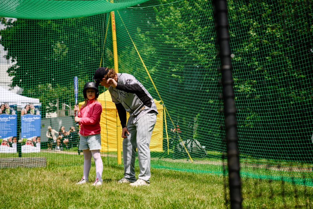 Ein Trainer erklärt einem Kind das Baseballspielen an einer Mitmachstation beim Sportfest Move & Groove.