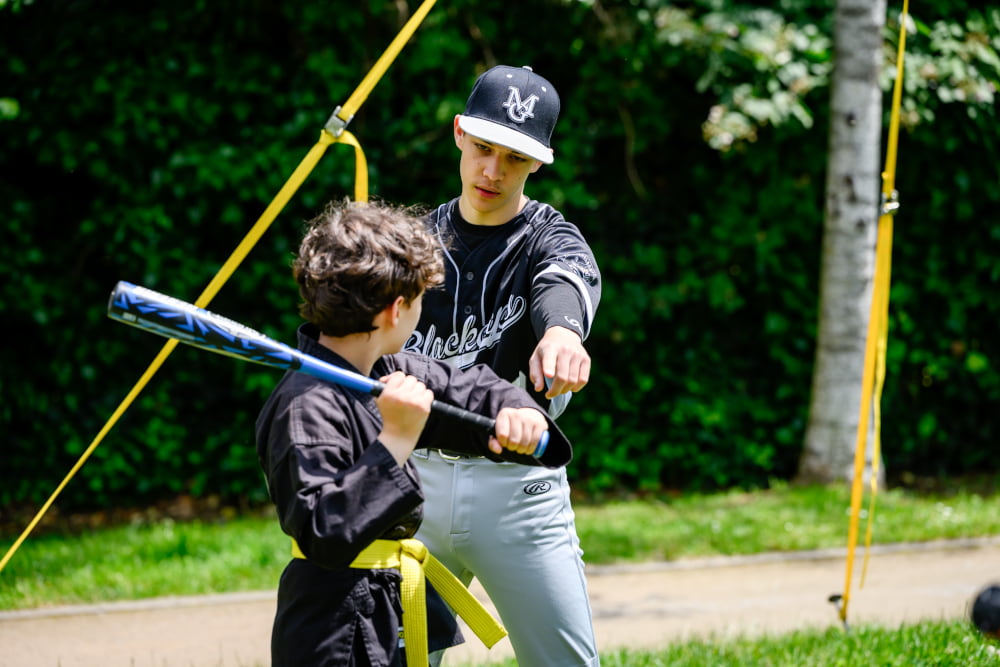 Ein Trainer zeigt einem Kind die richtige Schlagtechnik beim Baseball während des Sportfests Move & Groove.
